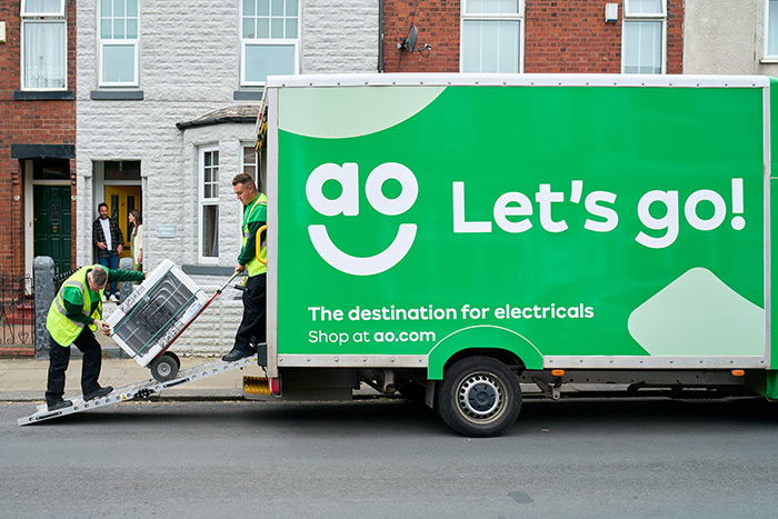 Two delivery drivers unloading a washing machine from an AO branded van